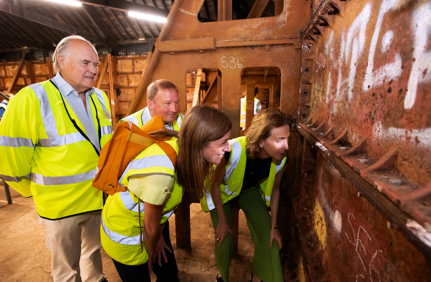 Two men and two men are pictured inside a metal-clad room, a huge disused water tank, and are peering at a crack through which daylight can be seen.