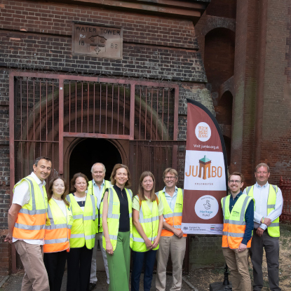 A group of smiling men and women stand in front of a brick building. 