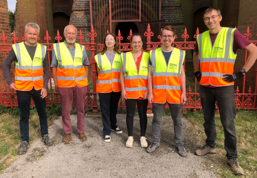 A group of smiling men and women stand in front of a brick building.